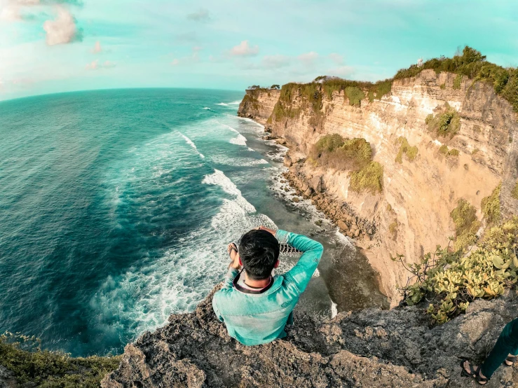 a man sitting on top of a cliff next to the ocean, pexels contest winner, avatar image, with teal clothes, bali, selfie photo