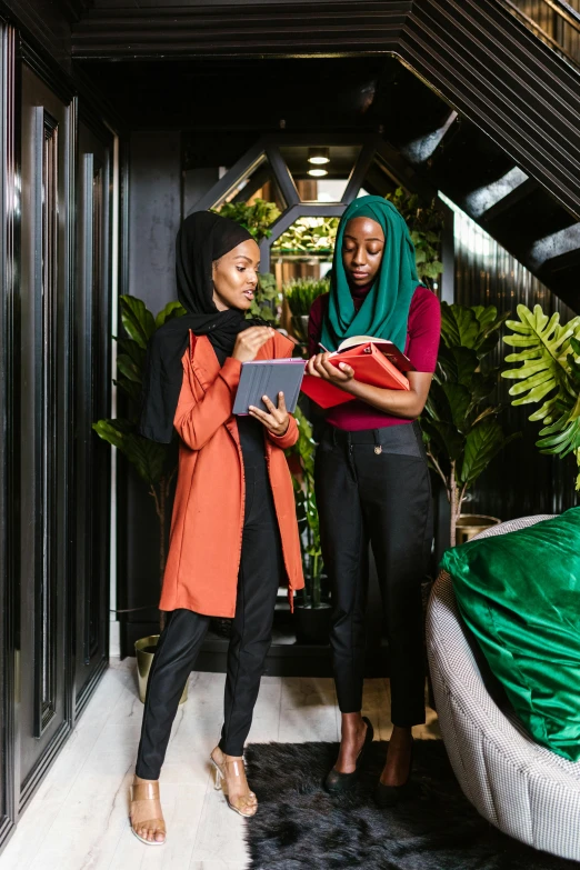 two women standing next to each other in a room, pexels contest winner, afrofuturism, holding notebook, islamic, inspect in inventory image, vibrant foliage