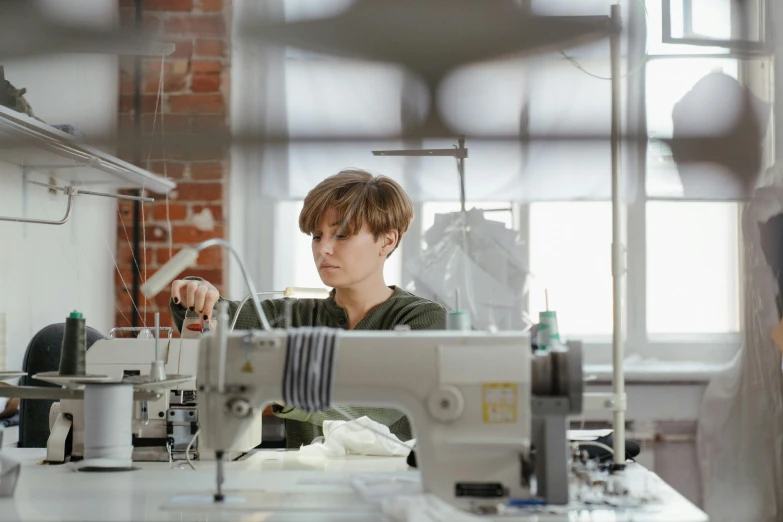 a woman working on a sewing machine in a factory, by Lee Loughridge, trending on unsplash, avatar image, architect, embroidered robes, thumbnail