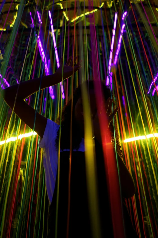 a person that is standing in front of some lights, inspired by Bruce Munro, interactive art, colored lasers, raver girl, hanging, intricate rainbow environment