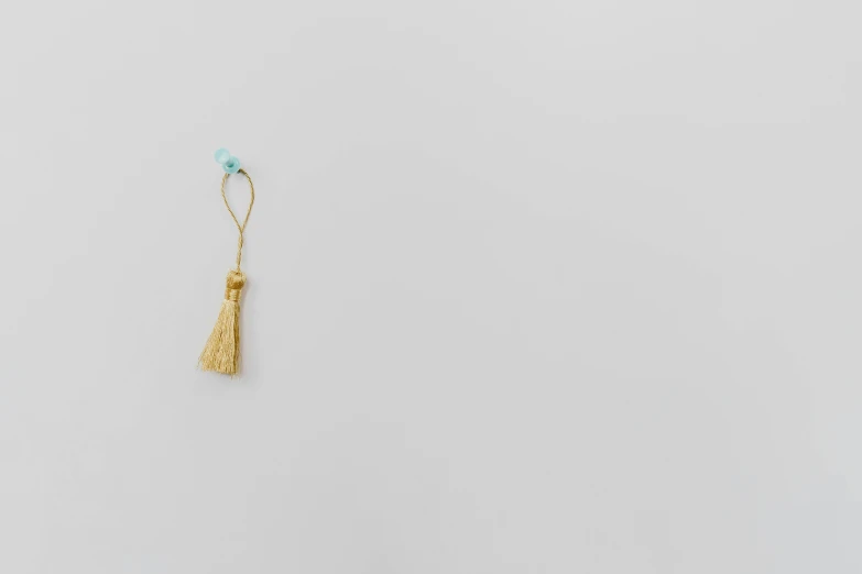a pair of earrings sitting on top of a table, by Makoto Aida, sōsaku hanga, tassels, minimalist photorealist, courtesy of moma, beige