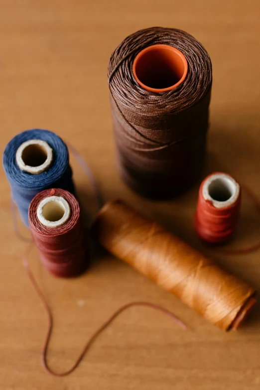 a couple of spools of thread sitting on top of a wooden table, leather and suede, indigo and red iron oxide, caramel. rugged, stitches