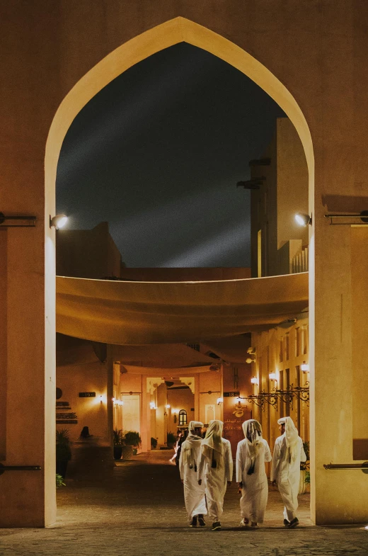 a group of men walking down a street at night, by Riad Beyrouti, giant majestic archways, ameera al taweel, mgm studios, courtyard