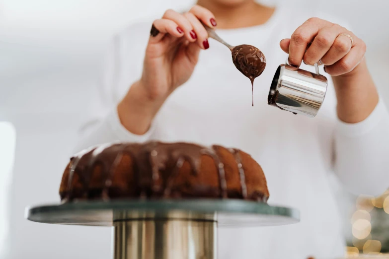 a woman sprinkles chocolate icing on a bundt cake, by Julia Pishtar, pexels contest winner, aussie baristas, pouring, made of liquid metal and marble, profile image