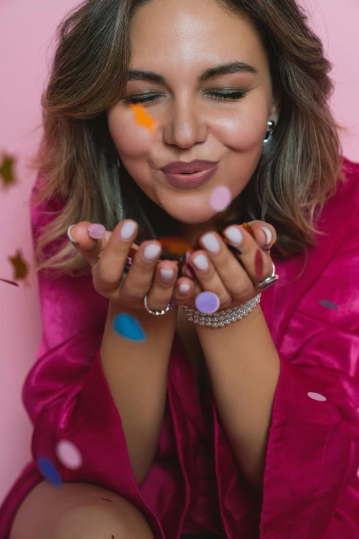 a woman in a pink robe blowing confetti, a colorized photo, trending on pexels, wearing two silver bracelets, wolfy nail, photoshoot for skincare brand, brightly coloured