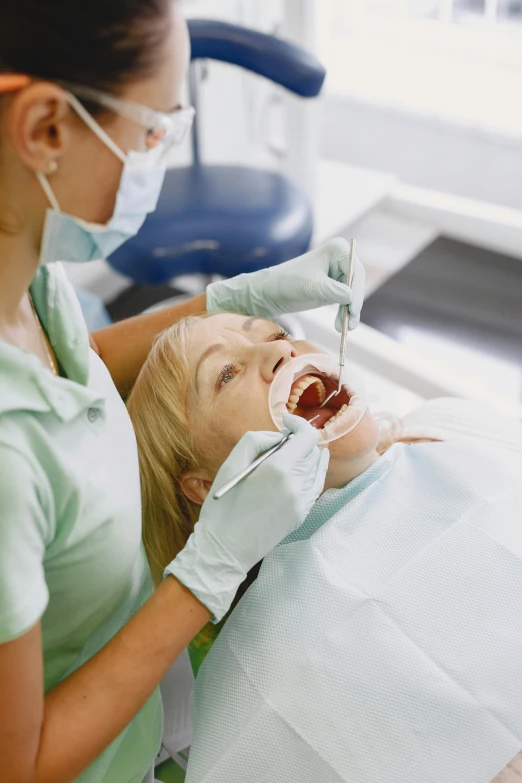 a woman getting her teeth examined by a dentist, by Elizabeth Durack, shutterstock, no cropping, single subject, high angle shot, scrubs