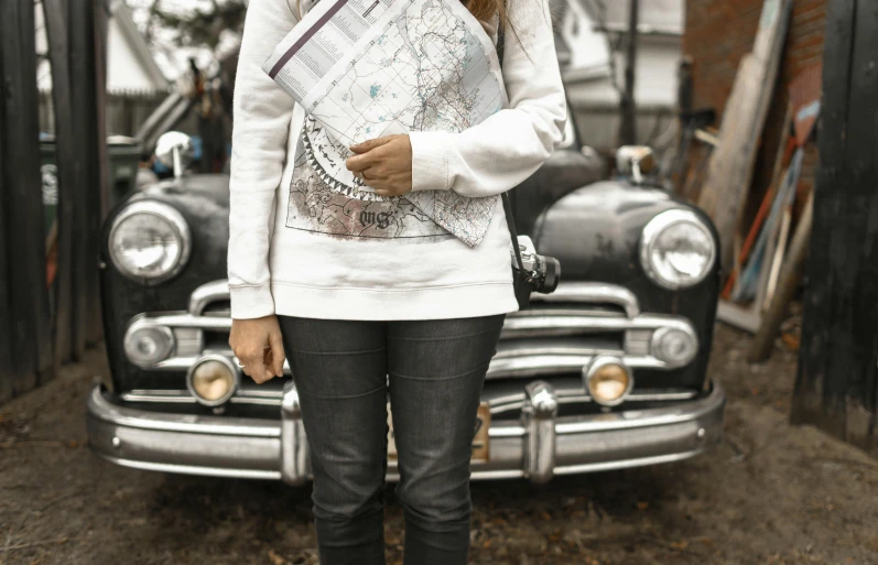 a woman standing in front of an old car, pexels contest winner, map cartography, wearing sweatshirt, holding a clipboard, detailed white