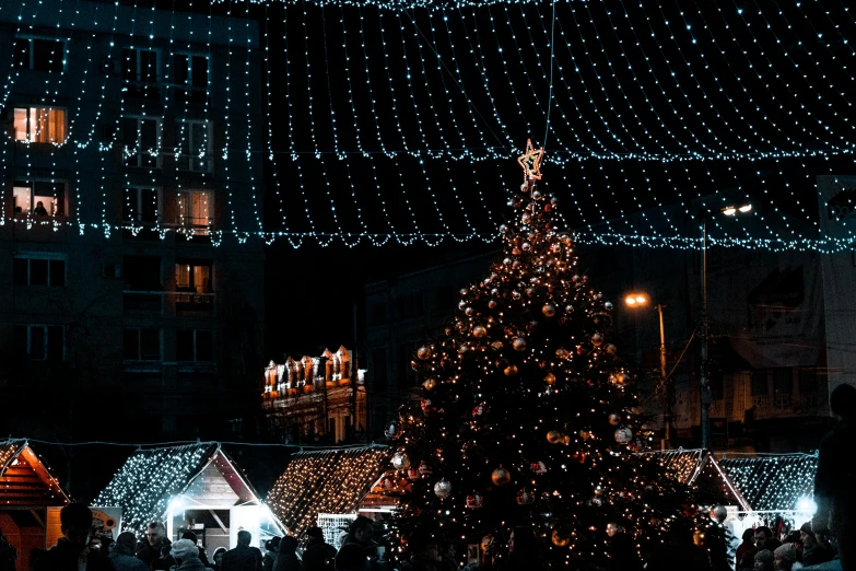 a group of people standing around a christmas tree, by Adam Marczyński, pexels contest winner, lush tress made of city lights, square, black, market