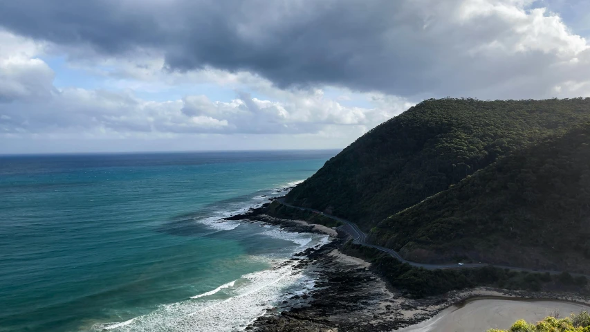 a view of the ocean from the top of a hill, by Anna Findlay, unsplash contest winner, bulli, landslide road, on a cloudy day, hilly road