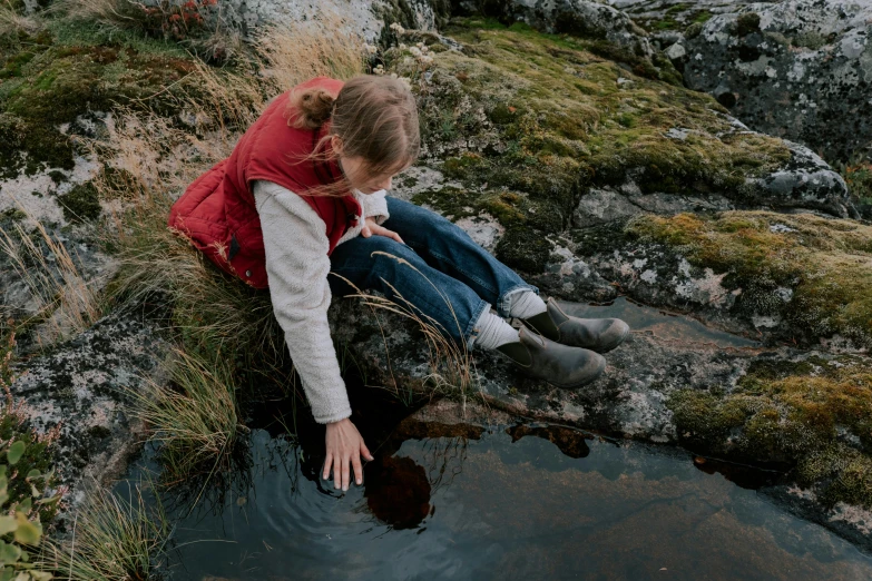 a woman sitting on top of a rock next to a body of water, filling with water, sadie sink, puddles of water on the ground, subsurface scandering