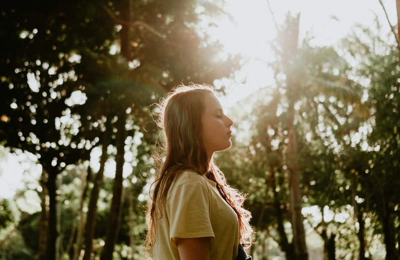 a woman standing in the middle of a forest, sun - drenched, girl with brown hair, portrait featured on unsplash, looking off into the distance