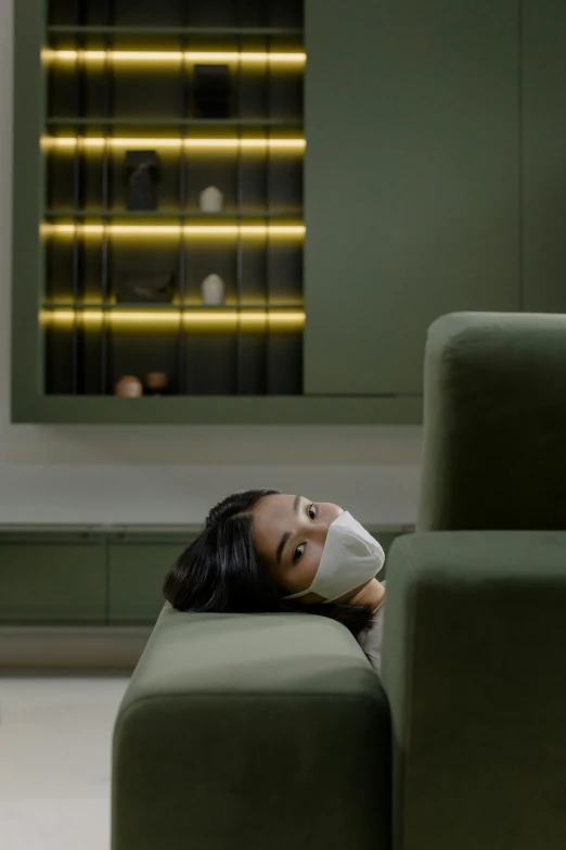 a woman laying on a couch with a face mask on, inspired by Fei Danxu, furniture, green facemask, waiting room, haze