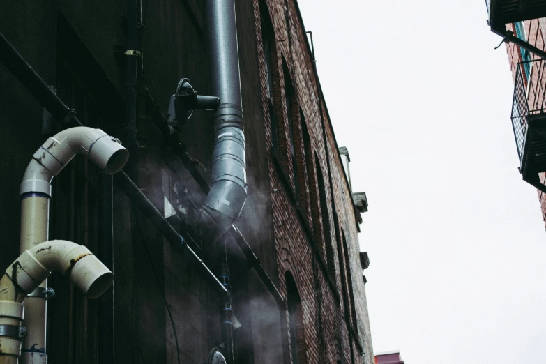 a couple of pipes that are on the side of a building, inspired by Elsa Bleda, pexels contest winner, fog machine, cyberpunk alley, awnings, tiny smokes from buildings