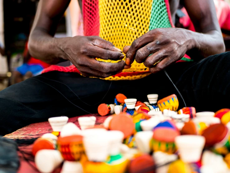 a man sitting in front of a pile of toys, west africa mask patterns style, the glass bead game, colourful close up shot, thumbnail