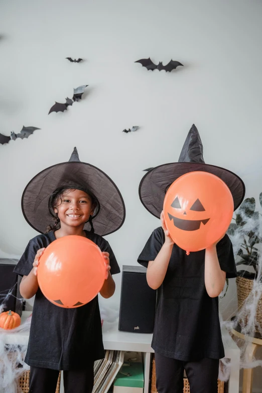 two children dressed up in halloween costumes holding balloons, pexels contest winner, vanitas, ( ( ( black witch hat ) ) ) ), decoration around the room, ☁🌪🌙👩🏾, high-quality photo