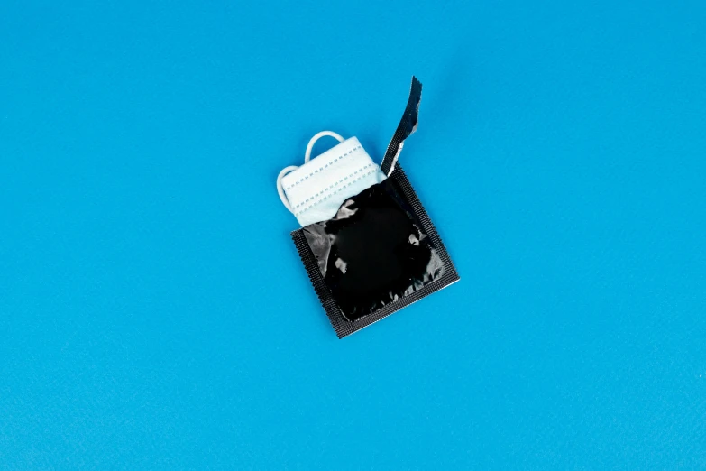 a black and white cellphone sitting on top of a blue surface, by Niko Henrichon, plasticien, bag - valve mask, contracept, opening shot, square