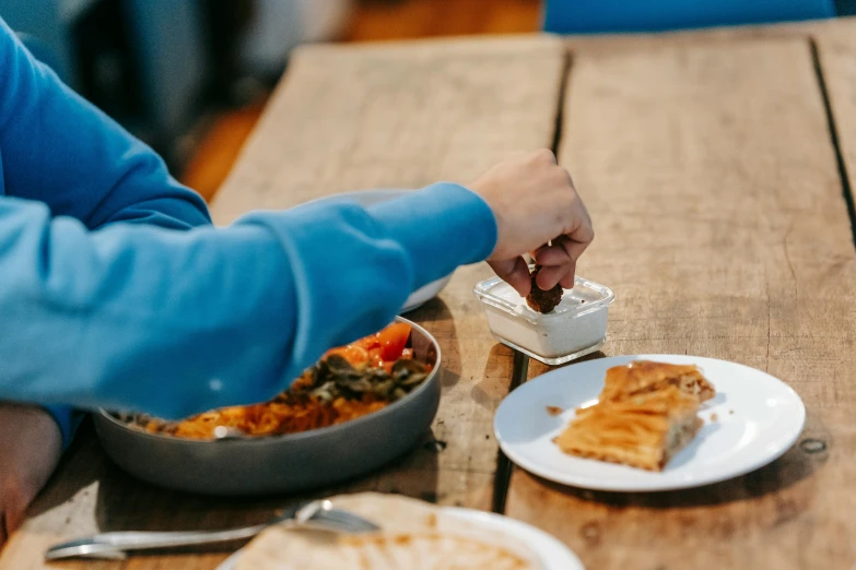 a person sitting at a table with a plate of food, pexels contest winner, hurufiyya, greek, holding a tin can, serving suggestion, on a wooden desk