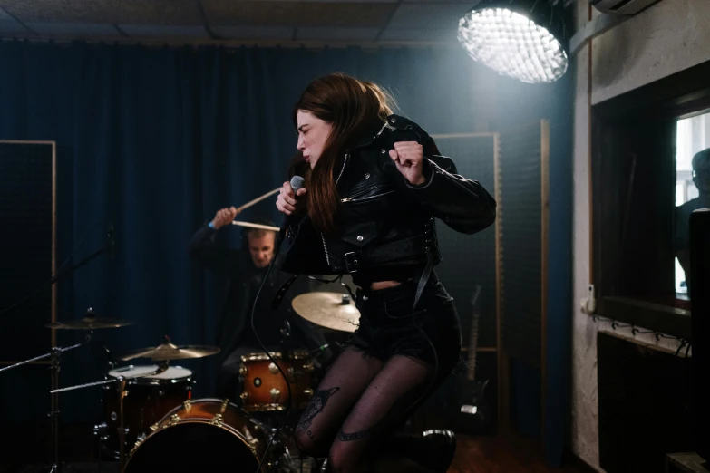 a woman sitting on top of a drum kit, pexels contest winner, antipodeans, singing into microphone, leather clothes, bassist, shaft studio