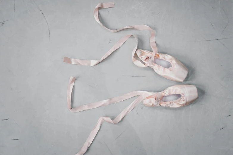 a pair of ballet shoes sitting on top of a floor, by Helen Stevenson, trending on unsplash, arabesque, ribbons, faded pink, on a gray background, made of glazed