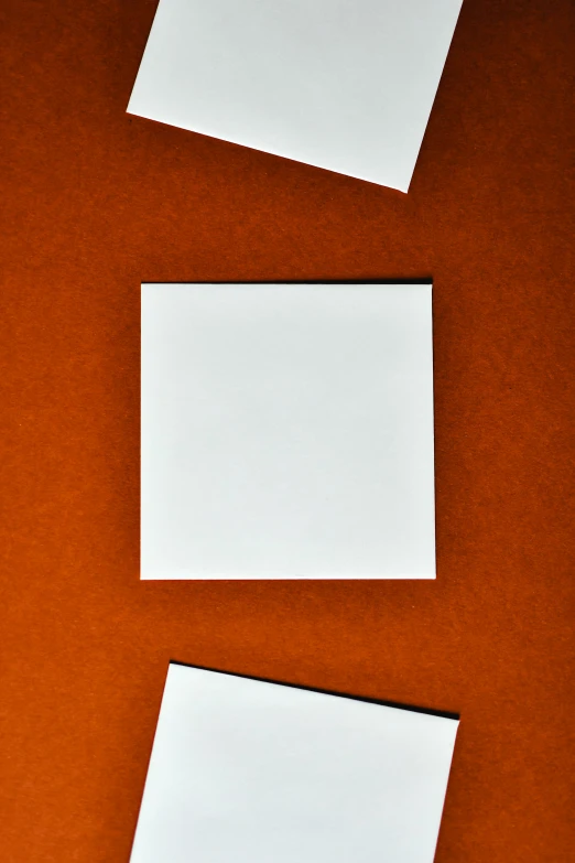 three pieces of paper sitting on top of a table, by Doug Ohlson, trending on pexels, postminimalism, square face, white and orange, symmetrical image, white