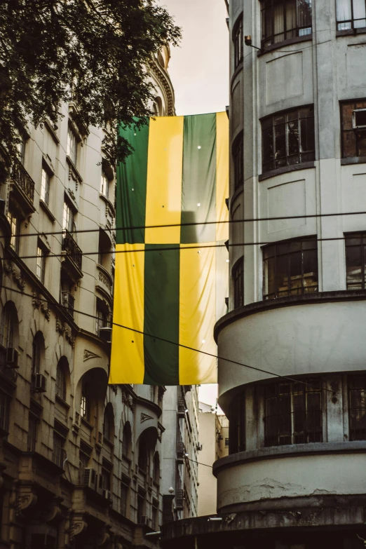 a yellow and green flag hanging from the side of a building, an album cover, by Fernando Gerassi, unsplash contest winner, sao paulo in the year 2 0 7 0, ignant, khreschatyk, cloth banners