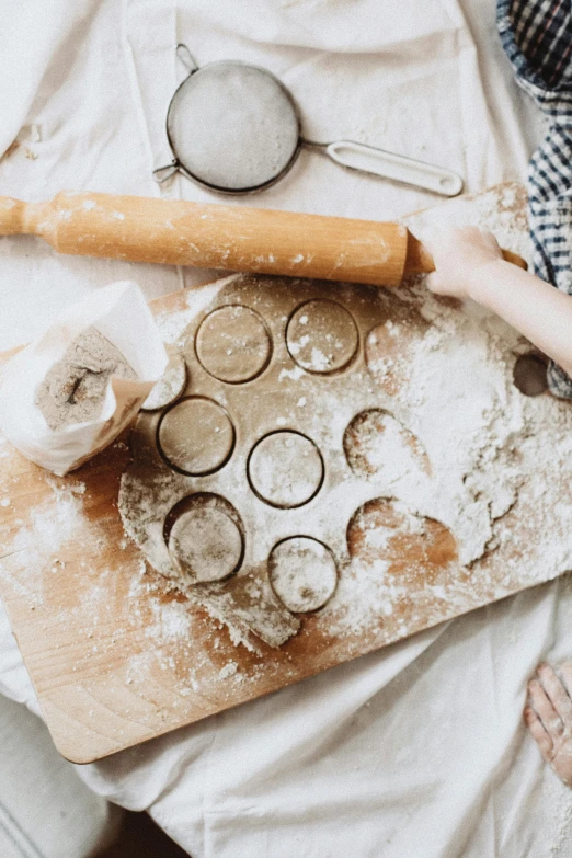 a person rolling out dough on a cutting board, by Sylvia Wishart, trending on unsplash, pots and pans, playful composition, pastries, 15081959 21121991 01012000 4k