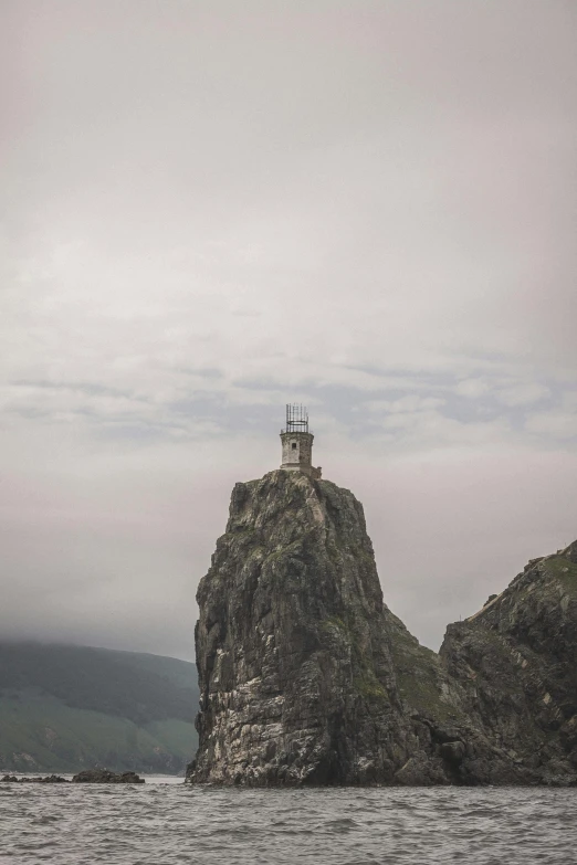 a lighthouse sitting on top of a rock in the ocean, on top of a mountain, grey skies, russian temple, eeyrie