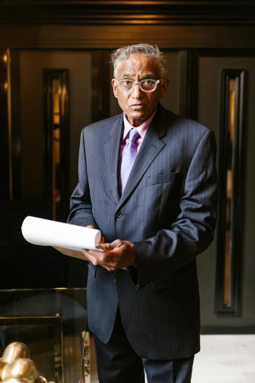 a man in a suit holding a roll of paper, ranjit ghosh, serious lighting, older male, holding notebook