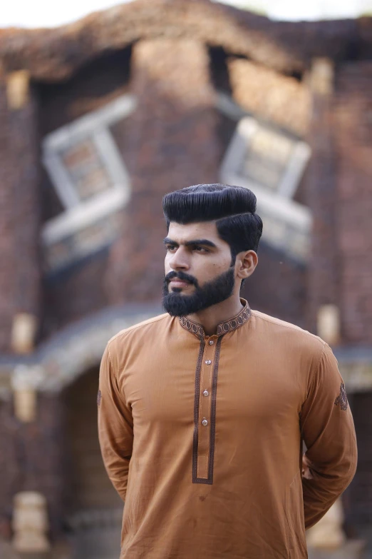 a man with a beard standing in front of a building, by Max Dauthendey, pexels contest winner, hurufiyya, wearing a kurta, brown buzzcut, beautiful young man, trending on artstion