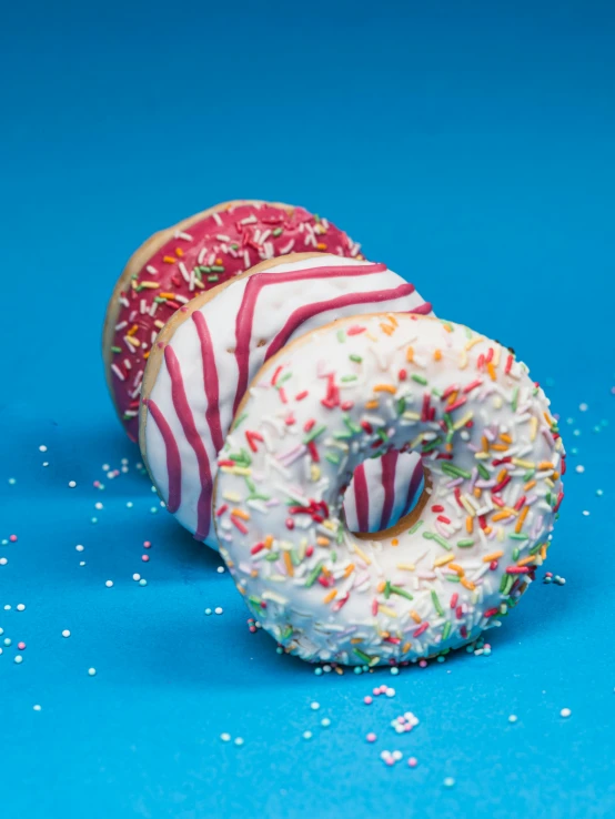 two donuts with sprinkles on a blue surface, a portrait, by Sebastian Spreng, unsplash, 15081959 21121991 01012000 4k, directional sunlight skewed shot, full body close-up shot, multilayer