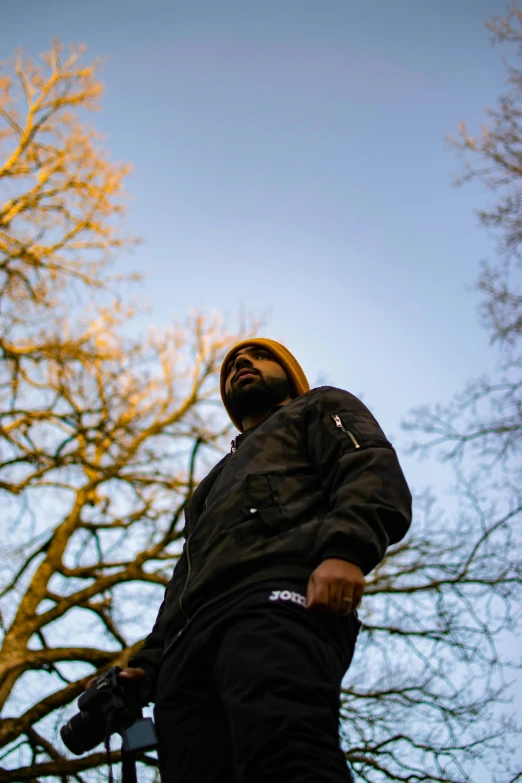 a man standing in front of a tree, an album cover, inspired by Oluf Høst, unsplash, low angle facing sky, ( golden hour ), ghostface, teddy fresh