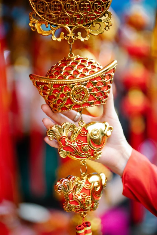 a close up of a person holding a gold object, inspired by Pu Hua, red lanterns, ornamental bow, hanging lanterns, market