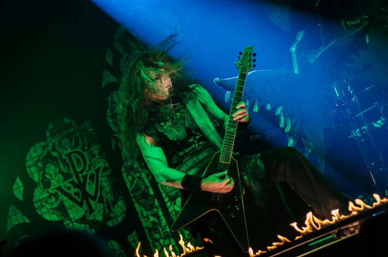 a man that is sitting down with a guitar, black metal rococo, very dark with green lights, headbanging, elaborate stage effects