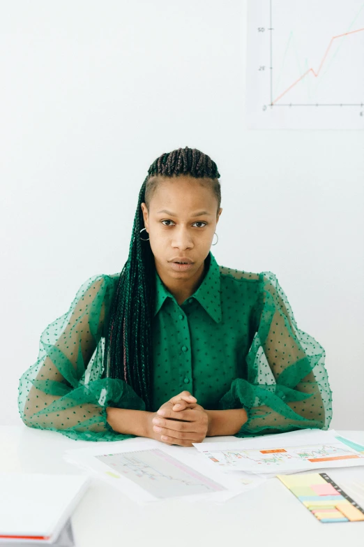 a woman sitting at a table with papers in front of her, green clothes, aida muluneh, set against a white background, green charts