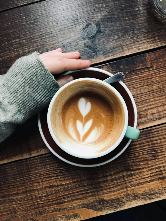 a person holding a cup of coffee on a wooden table, by Robbie Trevino, multiple stories, laura watson, cappuccino, abcdefghijklmnopqrstuvwxyz