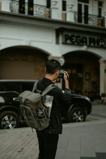 a man standing on the side of a street talking on a cell phone, pexels contest winner, photorealism, holding a dslr camera, a man wearing a backpack, grey, pixel perfect photograph