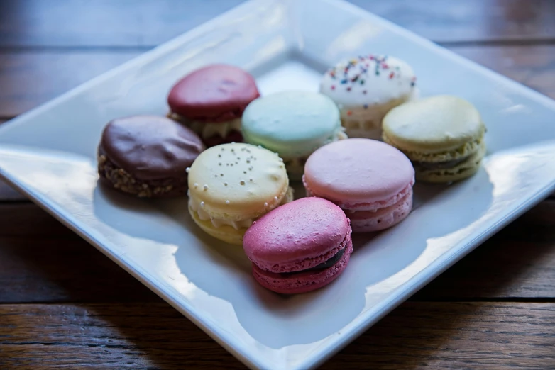 a white plate topped with macarons on top of a wooden table, 15081959 21121991 01012000 4k, square, ground - level medium shot, group photo