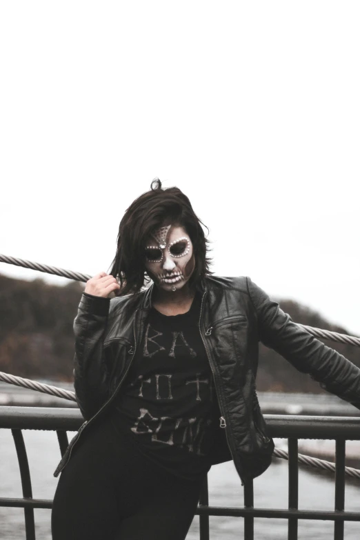 a woman standing on top of a bridge next to a body of water, inspired by Ren Bonian, trending on pexels, lowbrow, with black metal face paint, cute emo guy, dressed in leather jacket, ( ( ( skeleton ) ) )