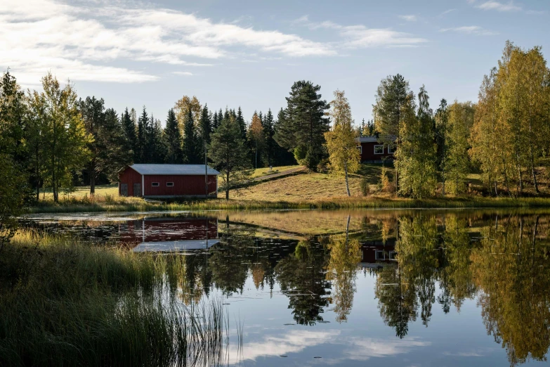 a red barn sitting on top of a lush green field, a picture, inspired by Eero Järnefelt, pexels contest winner, hurufiyya, trees reflecting on the lake, during autumn, wooden houses, exterior shot