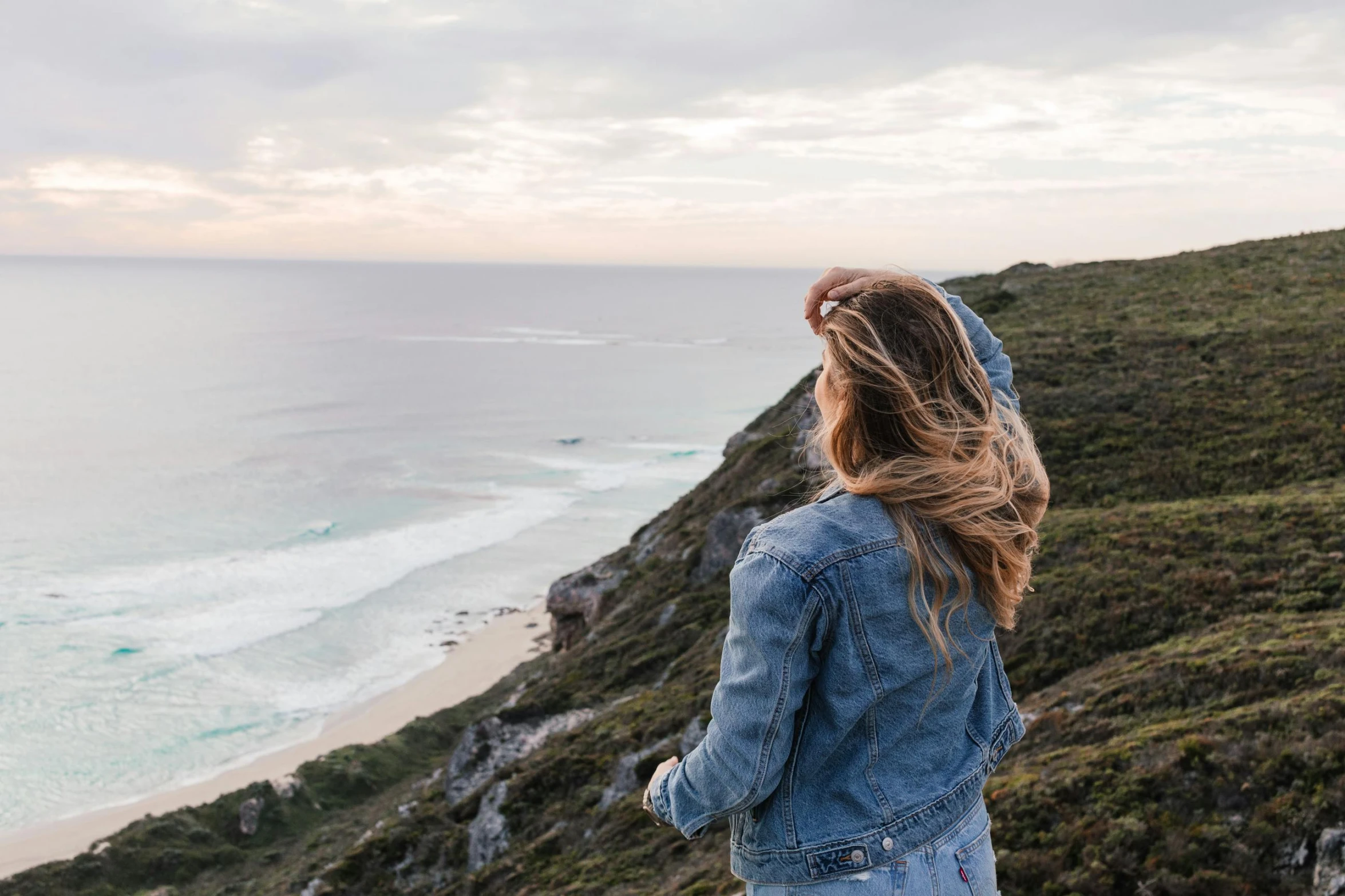 a woman standing on top of a hill next to the ocean, pexels contest winner, happening, wearing double denim, profile image, ocean spray, thin lustrous hair