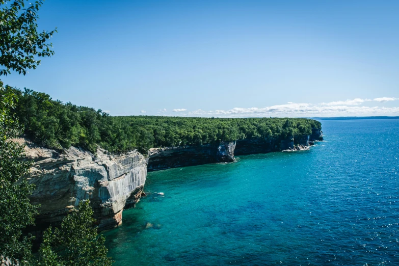 a large body of water surrounded by trees, by Kristin Nelson, pexels contest winner, coastal cliffs, michigan, blue water, tie-dye