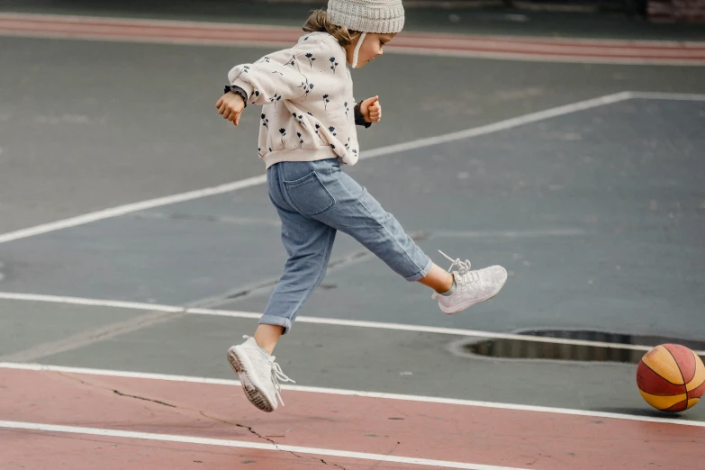 a little girl kicking a basketball ball on a court, by Anita Malfatti, pexels contest winner, blue jeans and grey sneakers, jumping for joy, wearing double denim, wearing a track suit