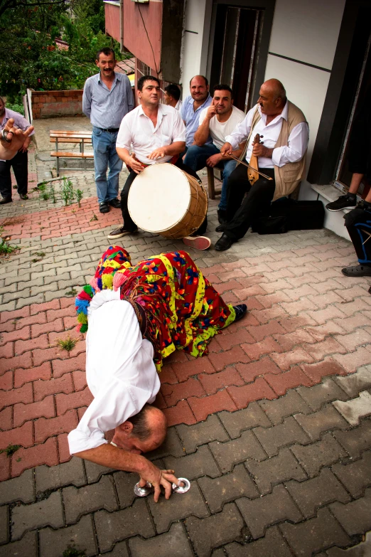 a group of people standing around a person laying on the ground, an album cover, by Ibrahim Kodra, pexels contest winner, traditional costume, playing drums, zelensky having a tantrum, 15081959 21121991 01012000 4k