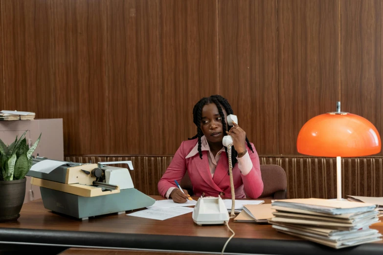 a woman sitting at a desk talking on a phone, an album cover, by Niels Lergaard, pexels contest winner, brown and pink color scheme, film still from the office, godwin akpan, museum curator