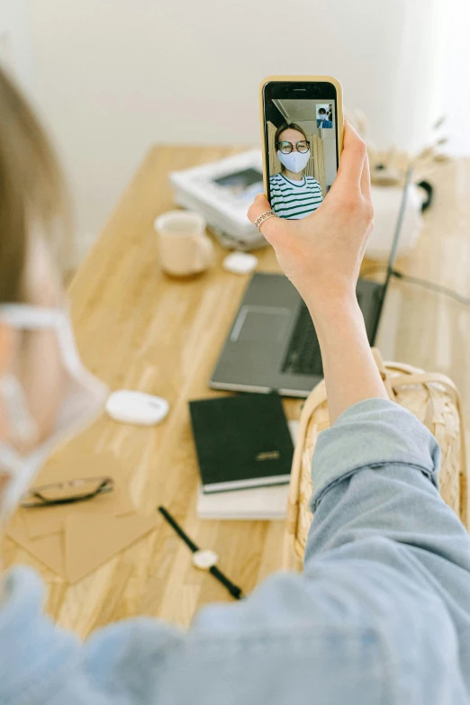 a woman taking a picture of herself on her cell phone, trending on pexels, sitting at desk, wearing facemask, home album pocket camera photo, a wooden