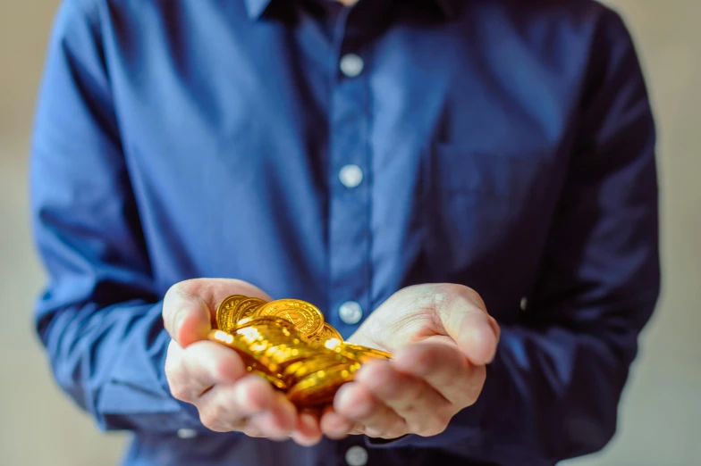 a man in a blue shirt holding a pile of gold coins, by Julia Pishtar, pexels, avatar image, high quality upload, image, taken on iphone 14 pro