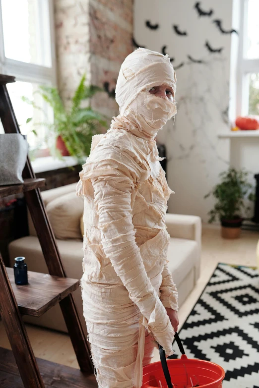 a man dressed as a mummy holding a bucket, inspired by Sarah Lucas, pexels contest winner, renaissance, at home, ripped fabric, movie filmstill, teenage girl