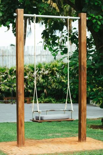 a wooden swing frame sitting on top of a lush green field, manila, in a beachfront environment, grey, rituals