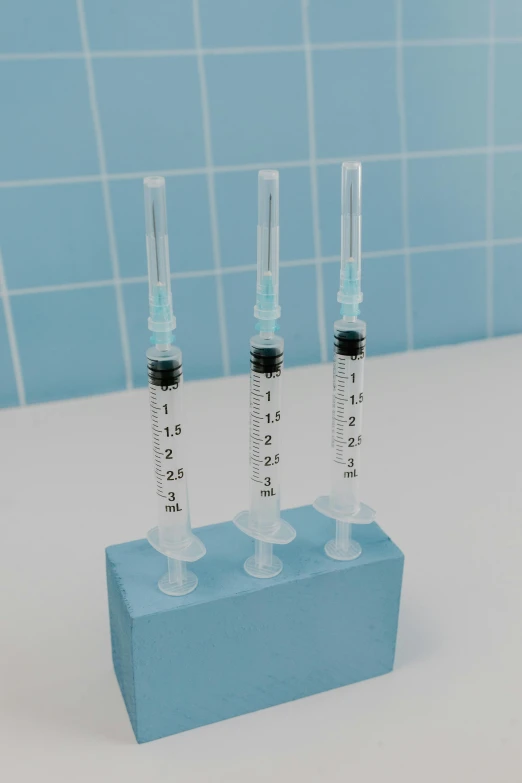 three vials sitting on top of a blue block, a 3D render, unsplash, showers, holding syringe, aesthetics, mini model