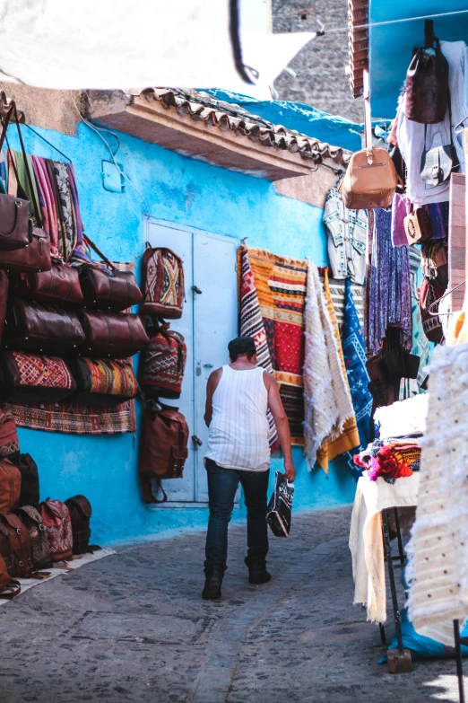 a woman walking down a street next to a blue building, crafts and souvenirs, areas rugs, 2019 trending photo, square